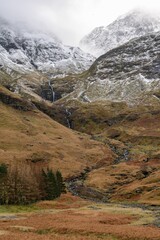 Vertical shot of snowcapped mountains in the Glencoe village in Glen Coe, Scottish Highlands - obrazy, fototapety, plakaty