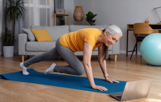 Online training at retirement. Senior woman doing mountain climbers exercise, watching online tutorial on laptop