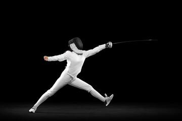 Energetic female fencer in white fencing costume and mask in action, motion isolated on dark background. Sport, youth, activity, skills, achievements, goal.