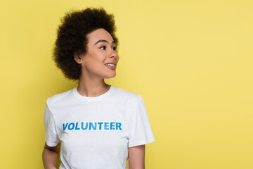 happy african american woman with volunteer lettering on t-shirt looking away isolated on yellow.