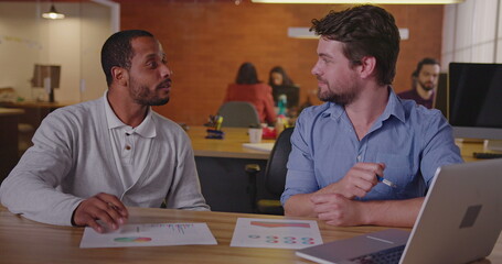 Two diverse millennial employees in front of laptop. A black colleague explains new job for a south American female employee. First day at new job concept