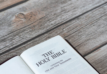 Open Holy Bible book containing the Old and New Testament on a rustic wooden table with copy space....