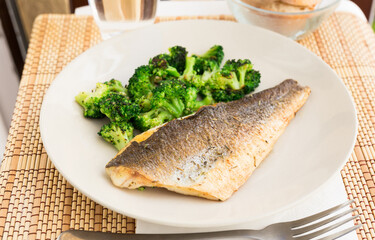 fried fillet of sea bass with garnish of broccoli on black warm stone plate