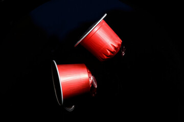 isolated red metallic aluminum coffee capsules on black glass surface.. modern lifestyle. fast and...