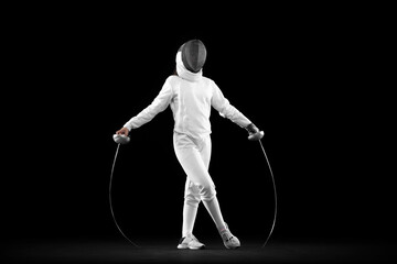 Young serious girl, beginner fencer in white fencing costume standing with rapier ans mask isolated...