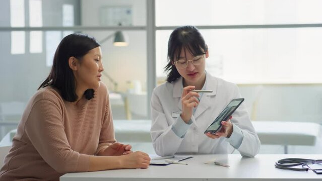 Asian female doctor showing chest x-ray image on digital tablet to woman while explaining diagnosis on medical consultation in clinic