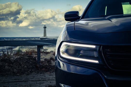 Closeup of a headlight of a black car parked at Sodus Bay, against a lighthouse