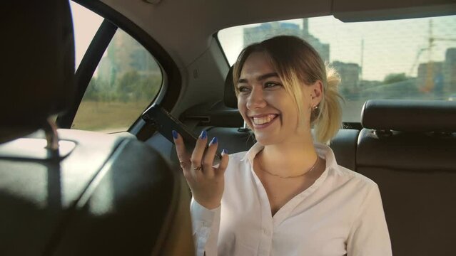 Young business woman in suit is recording a voice message on her smart phone in the back seat of her car. Riding car and holding phone on hand.Taxi lifestyle.Slow motion