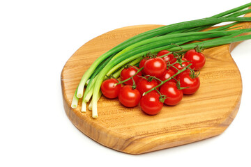 Bunches of fresh red cherry tomatoes and young green onion on cutting board isolated on white background. Ripe tomatoes on green stems. Bunch of fresh onion. Fresh organic vitamin vegetables.