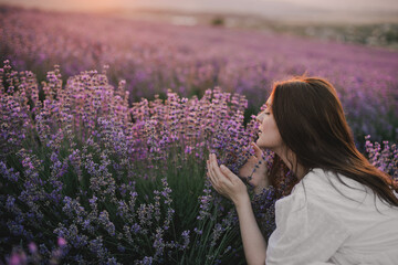 Young beautiful woman in white dress enjoying fragrance on lavender field.