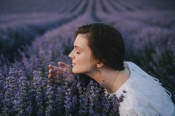 Young beautiful woman in white dress enjoying fragrance on lavender field. © polinaloves