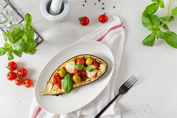 Italian traditional dish with eggplant, tomatoes, olives, mozzarella and basil. Baked aubergine stuffed with vegetables on a white plate. Vegan menu recipe. Top view, copy space