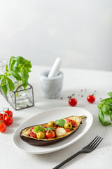 Grilled eggplants with mozzarella, tomatoes, basil and olives on a plate on white background. Aubergine seasonal vegan recipe. Dieting, healthy nutrition. Restaurant menu. Side view, copy space