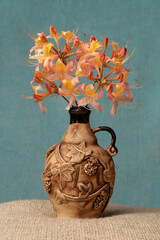 A sprig of rhododendron flowers in a clay jug. Grey background. Spring. Spring still life. Tranquility and comfort. Light, soft. Sackcloth. Vintage. Simple and beautiful. In retro style. 