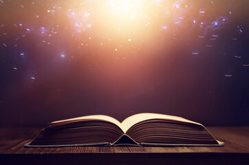 image of open antique book on wooden table with glitter overlay