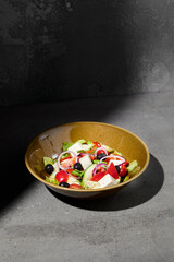 Classic greek salad on ceramic bowl in minimal style. Simple composition with greek salad on gray stone background with hard shadow. Dark concept menu. Vegetable salad on concrete table and shadow.