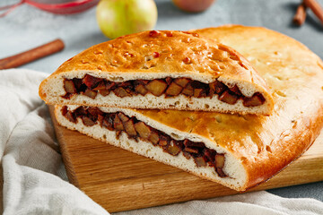 Sweet pie with apple on wooden board. Composition with apple pie on concrete background with textile and spices. Homemade pie with apple and cinnamon in rustic style on gray table.