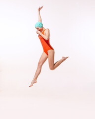 Portrait of young woman in swimming suit and cap jumping into water isolated over grey studio...