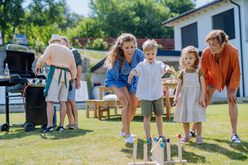 Multi generation family playing throw a ring game when grilling outside on backyard in summer at garden party.