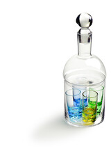 Kit with four glass shots with green and blue bottoms inside an empty glass liquor bottle, isolated on white