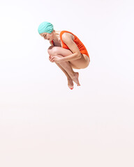 Portrait of young woman in swimming suit and cap jumping into water isolated over grey studio background. Dive-bombing