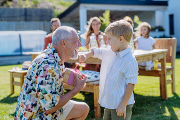 Happy little boy giving birthday present to his senior grandfather at generation family birthday...