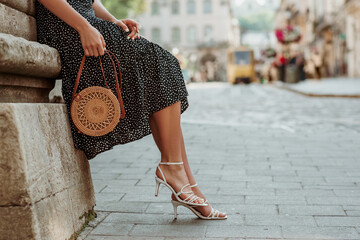 Trendy summer rotan wicker bag, white strap sandals in stylish female outfit. Woman posing in...