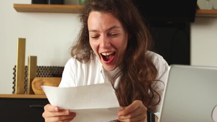 Happy brunette girl opening paper correspondence letter, reading good news, celebrate professional achievement success,sitting at desk with laptop at home.Excited satisfaction with bank loan approval