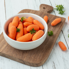 Baby carrots in a bowl over wooden table with herbs