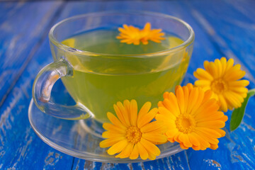 Calendula tea in a transparent cup on a blue background.Close-up.
