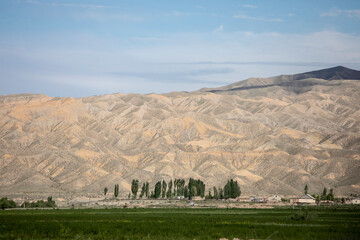 View of desert badlands in Kyrgyzstan with irrigated farmland in the foreground.