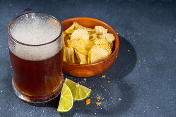 Beer with various salted snacks set. Black table background with traditional party snacks, beer bottles and glasses, with chips, onion rings, salted nuts, crisps and sauces top view copy space