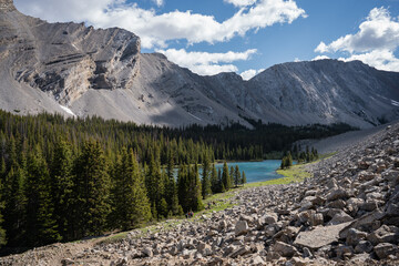 Fototapeta premium Just beyond the reach of a rockslide an incredible vivid blue mountain lake rests in the valley. all around the remarkable lake mountain peaks of the Canadian Rockies stand tall and proud. 