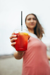 Selective focus on a glass of soft drink with ice in the hand of a young hipster girl - offers to drink
