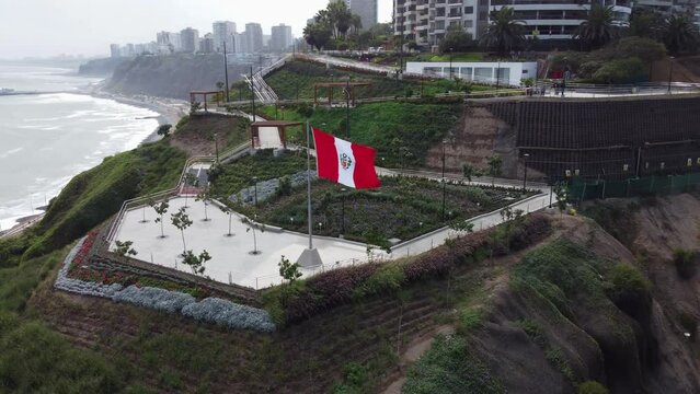 Drone video of "Parque Bicentenario" park in Miraflores, Lima, Peru. Park is on edge of the cliff, walk paths lead down to a big peruvian flag. Drone orbits the park revealing the coast and ocean.