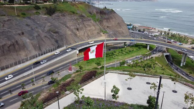 Drone footage of a park called "Parque Bicentenario" in Miraflores district of Lima, Peru. Drone flies forward over a big peruvian flag. Freeway overpass and cars can be seen and ocean in the distance