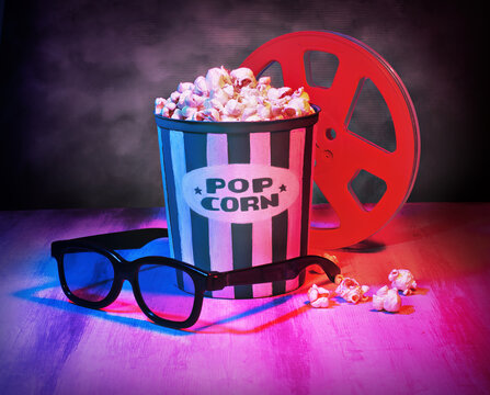 Cinema movies concept with a pop corn bucket, 3D glasses and film tape reel. Movie night template symbol table top shot, with a purple lights retro aesthetic