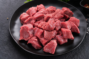 Raw chopped beef meat. Raw organic meat beef or lamb, spices, herbs on black plate on dark grey concrete background. Goulash. Raw uncooked meat. Meat with blood. Top view with copy space.