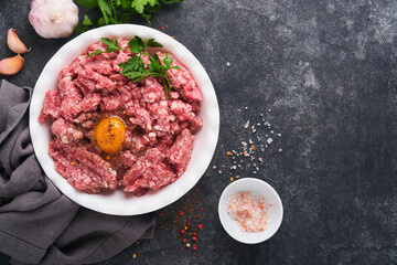 Raw minced meat. Ground meat beef, pork or lamb spices, herbs and eggs on white plate on black old concrete background. Fresh minced meat ready for cooking. Food cooking background. Top view.