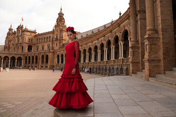 Beautiful teenage woman dancing flamenco in a square in Seville, Spain. She wears a red dress with...