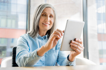 60s older mature woman sit in office and use digital tablet