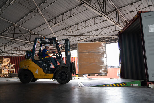 Warehouse worker driver in uniform delivery and loading pallet product by forklift.