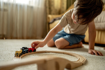 a boy at home in a room is building a railway, a child is playing with a toy train. Educational toys for home and kindergarten. Wooden Environmental Toys