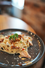 Tasty appetizing classic italian spaghetti pasta with creamy sauce, cheese parmesan and basil on plate on dark table at cafe restuarant. 