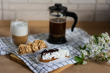 Hot cappuccino homemade beautiful layer white and layer of coffee black small coffee pot with espresso two eclairs with white whipped cream and brown whipped condensed milk and peanuts 