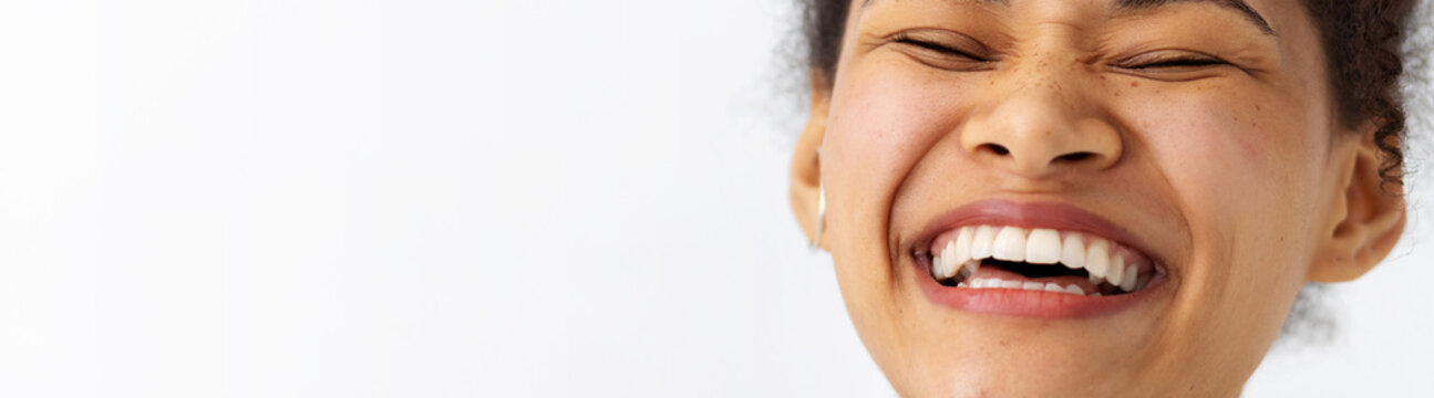 Portrait young happy positive African American woman with white teeth smiling broadly keeps eyes closed on white background, good mood concept, banner