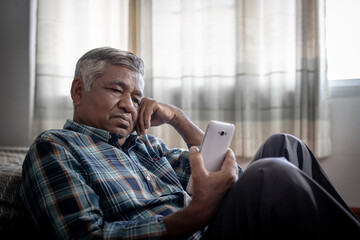 lonely elderly man sitting alone on bedroom and looking at phone - obrazy, fototapety, plakaty