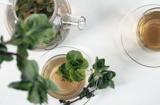 Fragrant mint tea on a light background. Glass teapot, a cup of tea, a bunch of fresh mint. Herbal tea application concept.