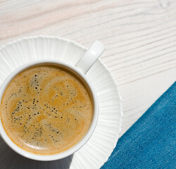 A cup of coffee and a saucer on a white table.
