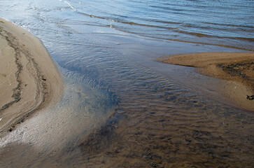 A top view of the bed of a small stream flowing into the lake. Beautiful drawing at the bottom of a stream of sand.